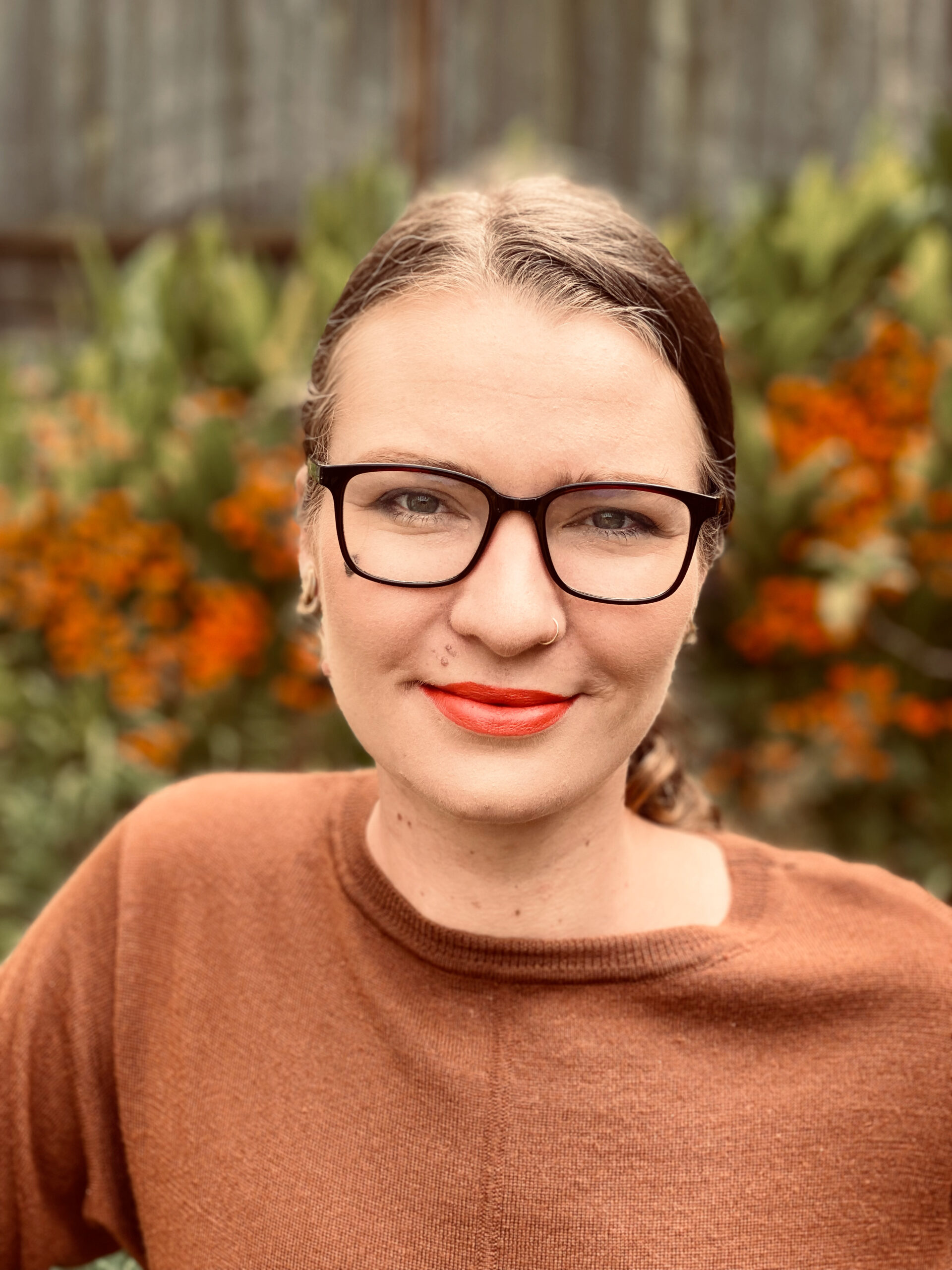 Headshot of Megan Sullivan-Tuba, a white woman with glasses and brown hair pulled back. She is wearing red lipstick and a brownish-red sweater.