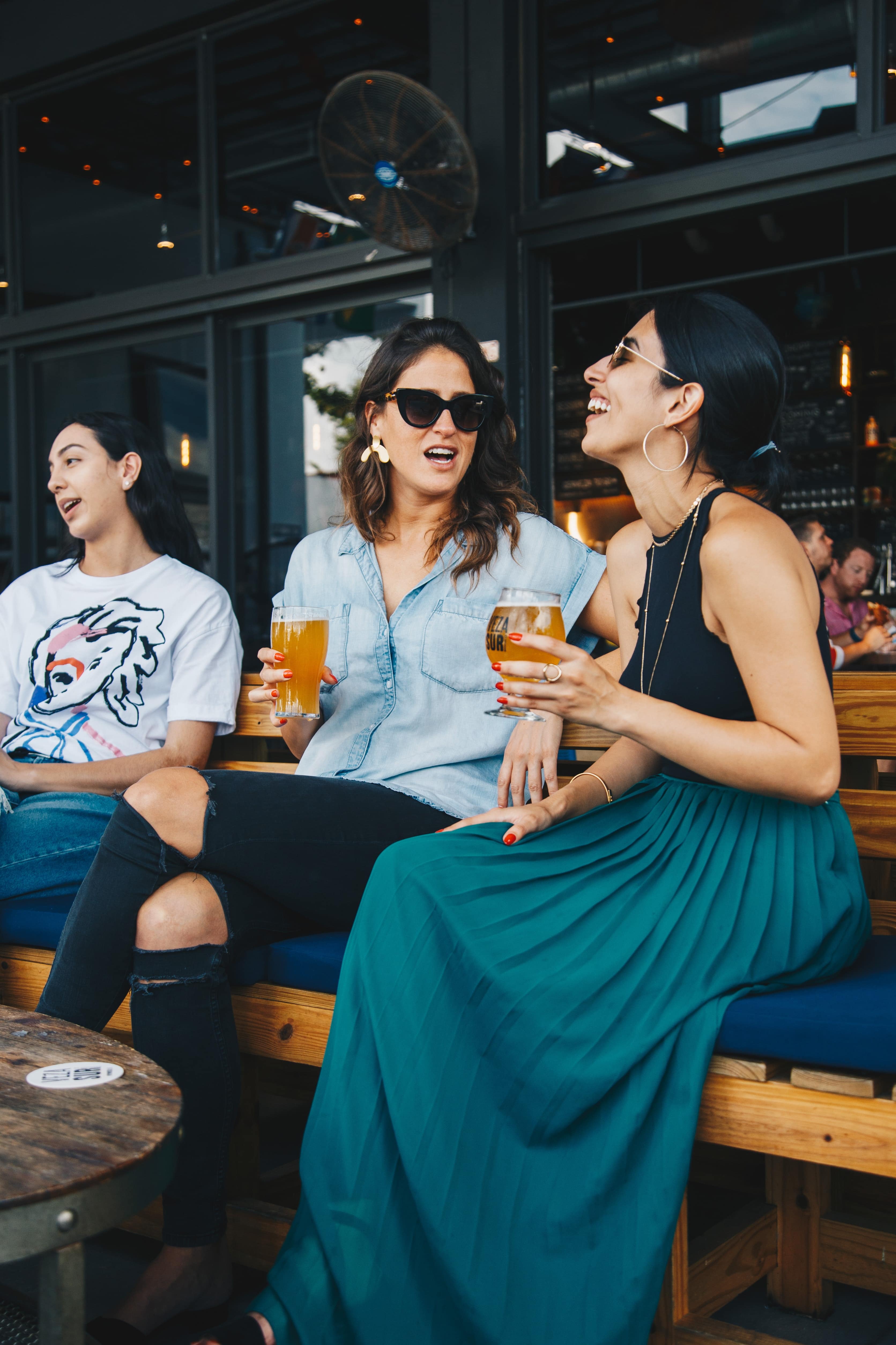 Group of friends hanging out on the patio at a bar, with beers in hand.