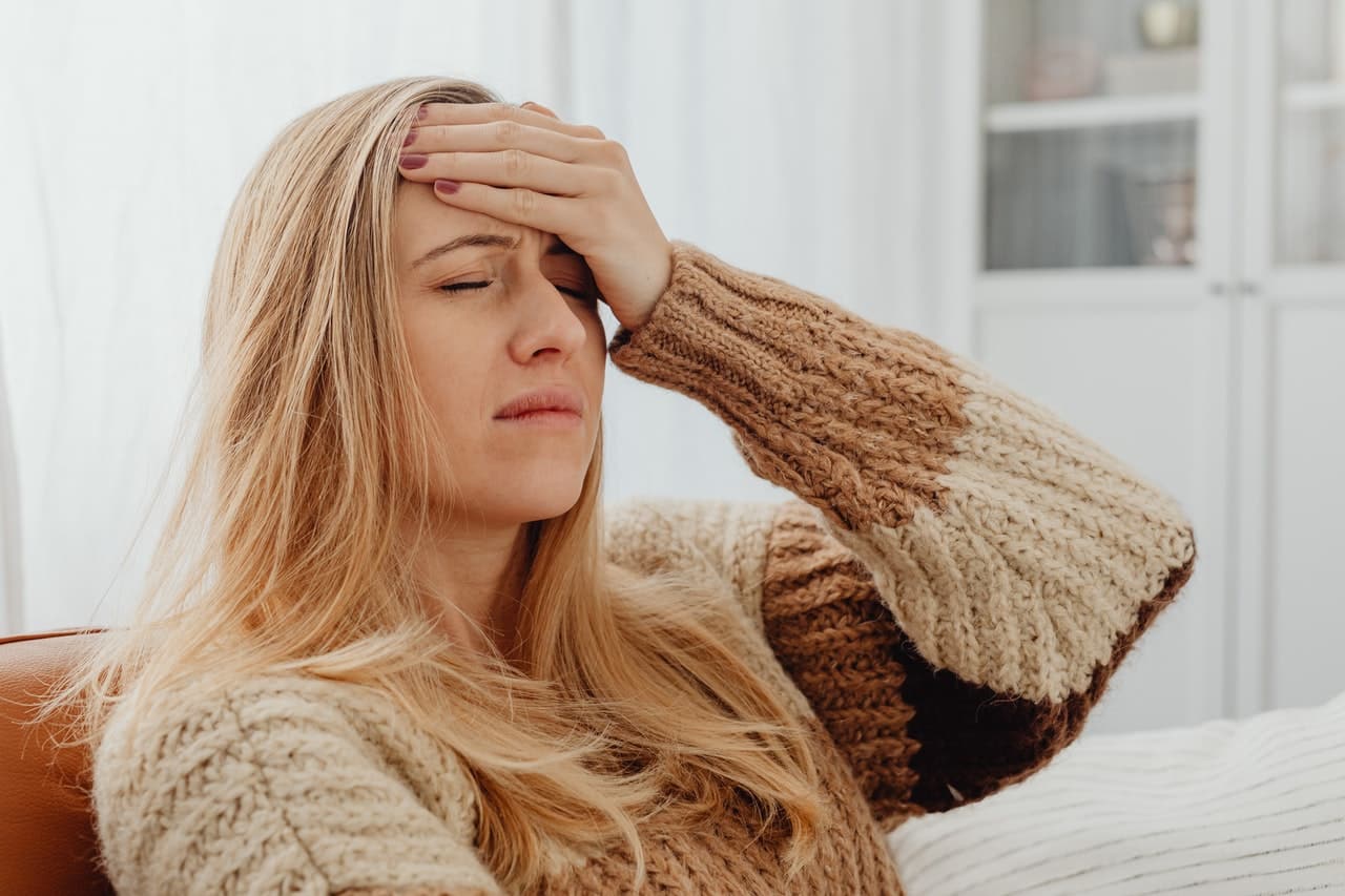 A blonde woman holds her hand to her forehead as though she is experiencing a headache or a migraine.