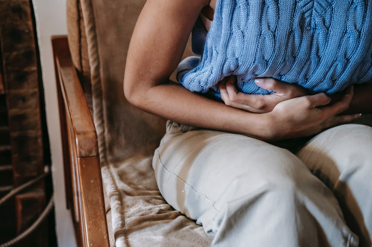 Photo of the torso of a person experiencing chronic stomach pain, with arms folded around their midsection.