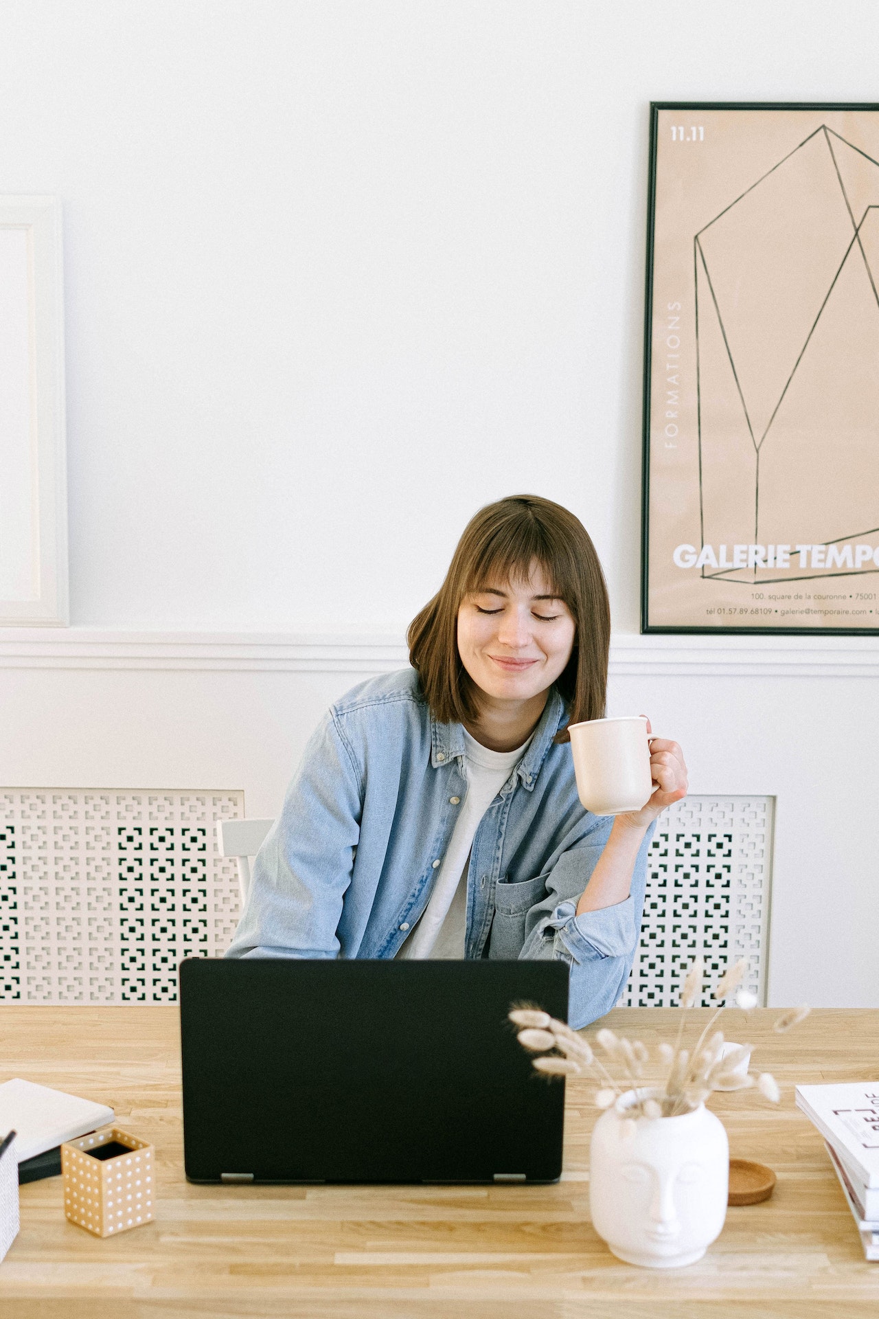 Happy woman with brown hair and bangs drinks coffee while working on a laptop