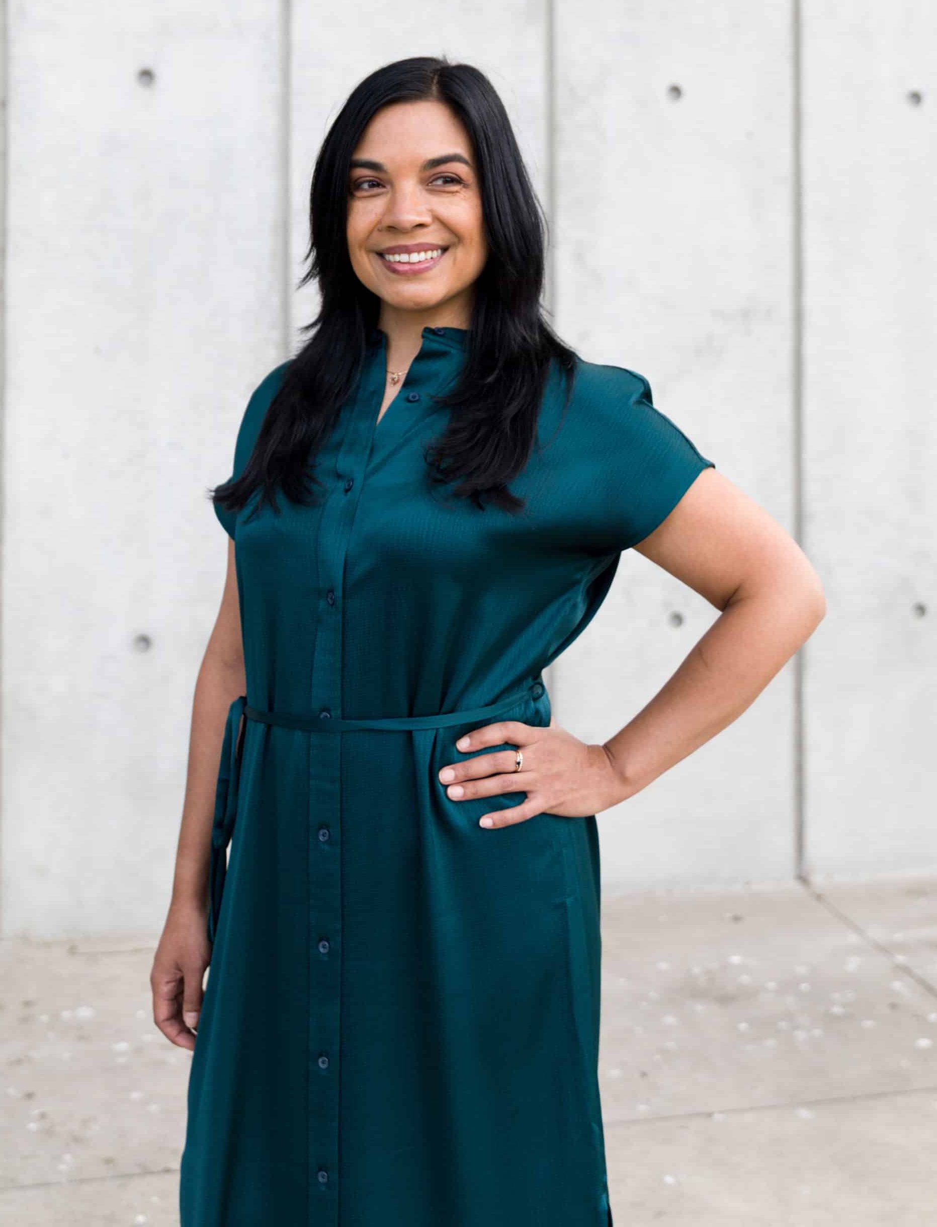 San Francisco psychologist Maya Borgueta, posing outdoors in front of a concrete wall. She is a Filipino woman in her early 40s with long dark hair and is wearing a dark green dress.