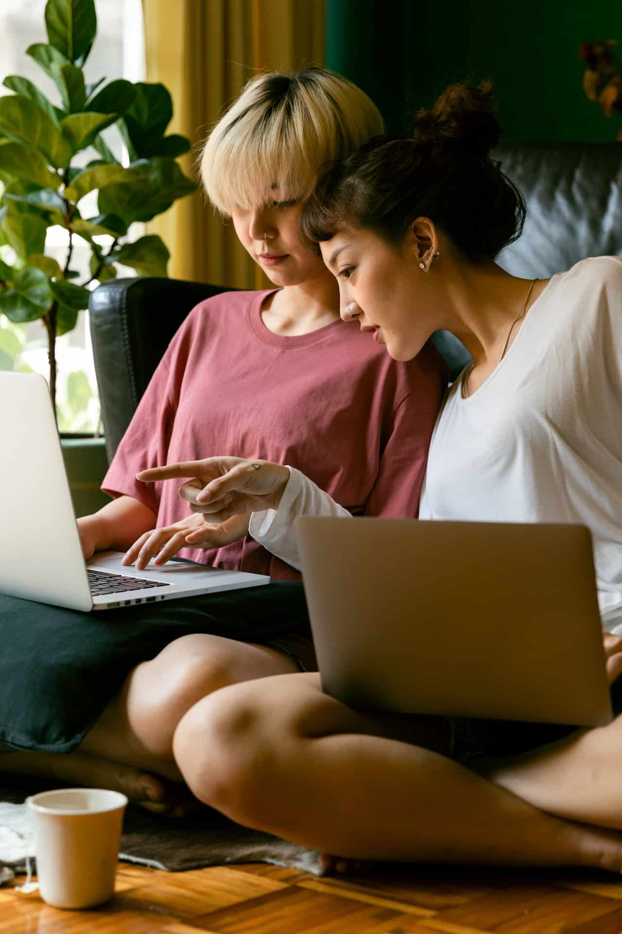 A queer couple sits on a sofa working together on their laptops.