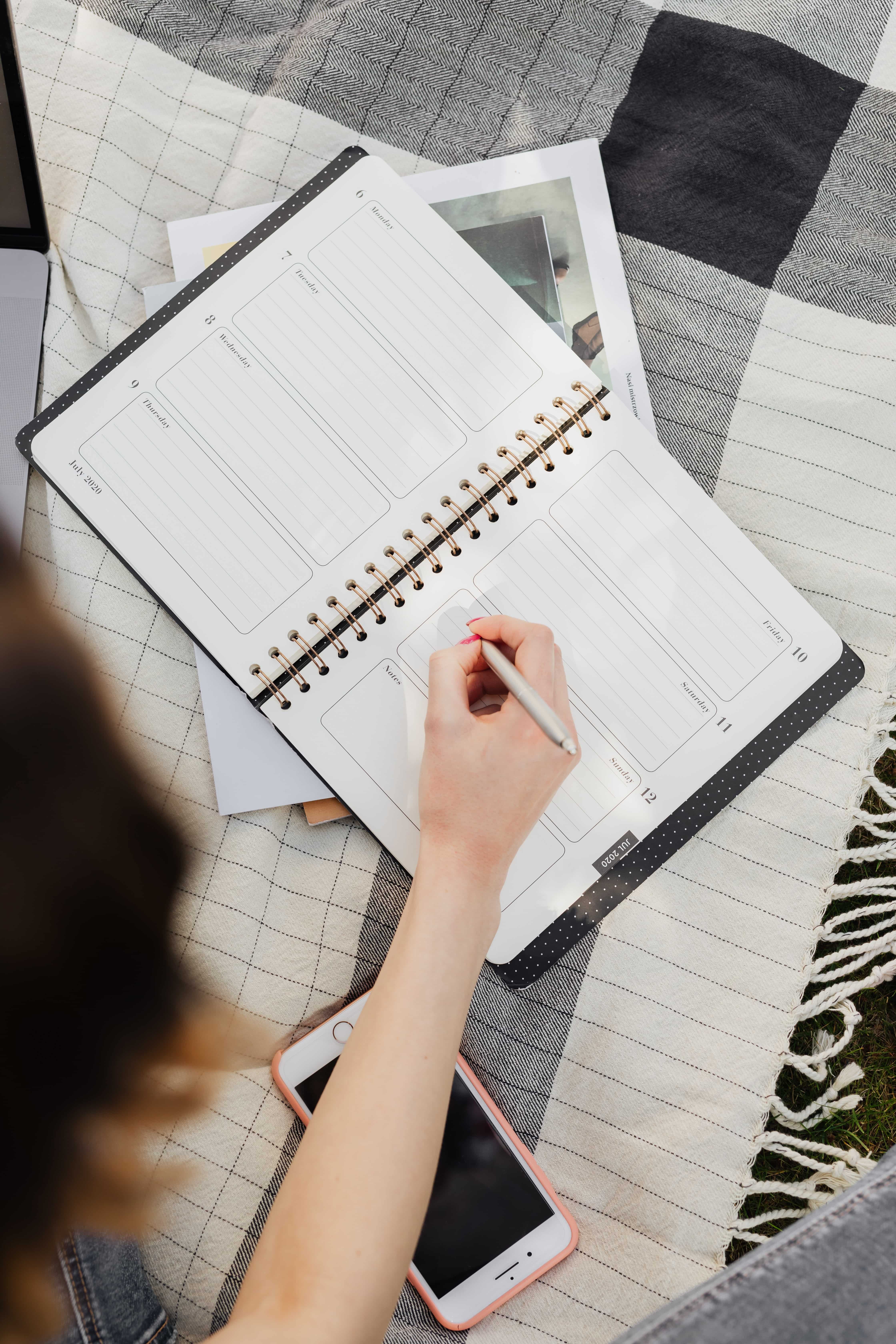 A planner open on a black and white blanket, photographed from above. A hand writing and part of a person's hair is visible.