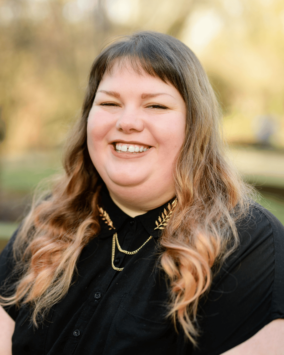 Headshot of Sage Swiatek, ACSW, online therapist serving clients in California. Sage is wearing a black shirt and has long, light brown hair with bangs. She is in an outdoor location, smiling at the camera. 