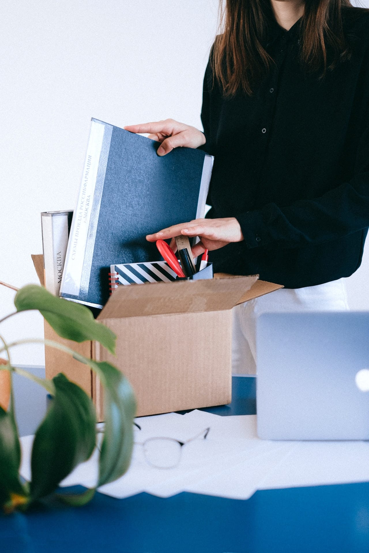 Photo of a woman's torso as she packs up a box of office supplies, as though she has just been laid off.