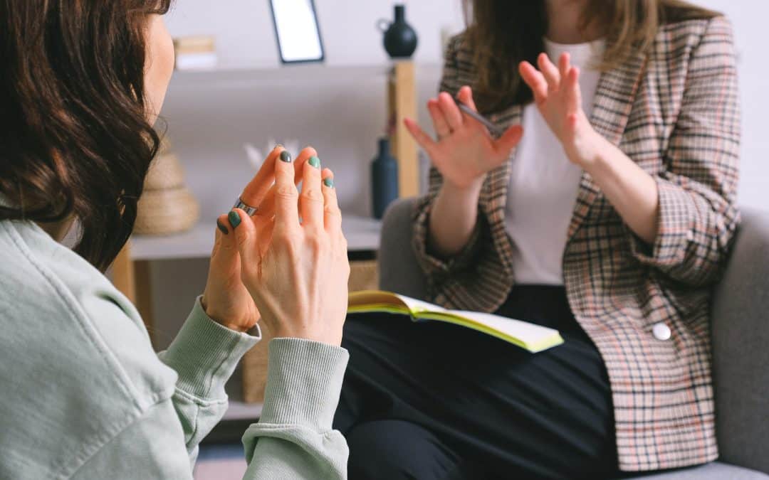 Two women sitting and talking in what appears to be a therapy session. Their faces are out of frame and they are gesturing their hands.