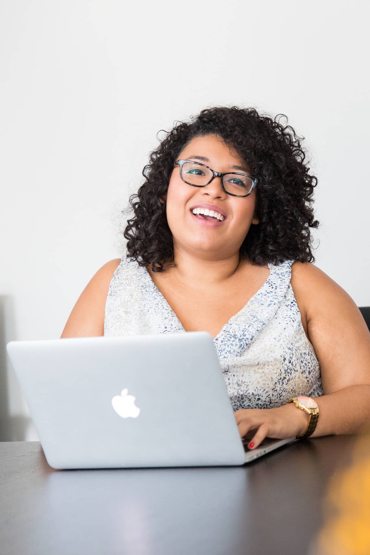 Latina woman sitting in professional attire in front of a laptop, looking happy.