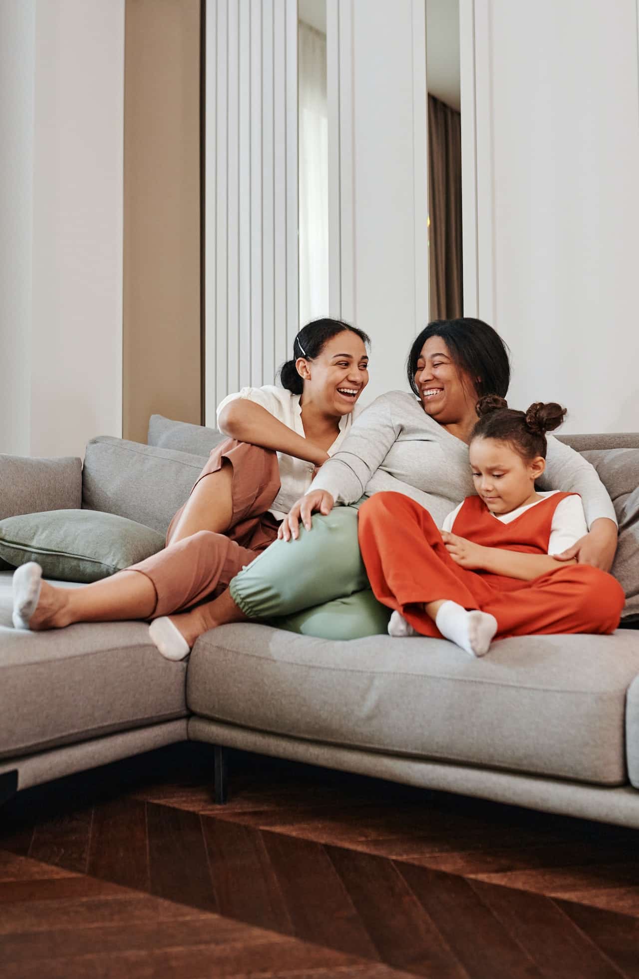 A family sits together on a couch, two women and a girl, looking happy and smiling at each other.