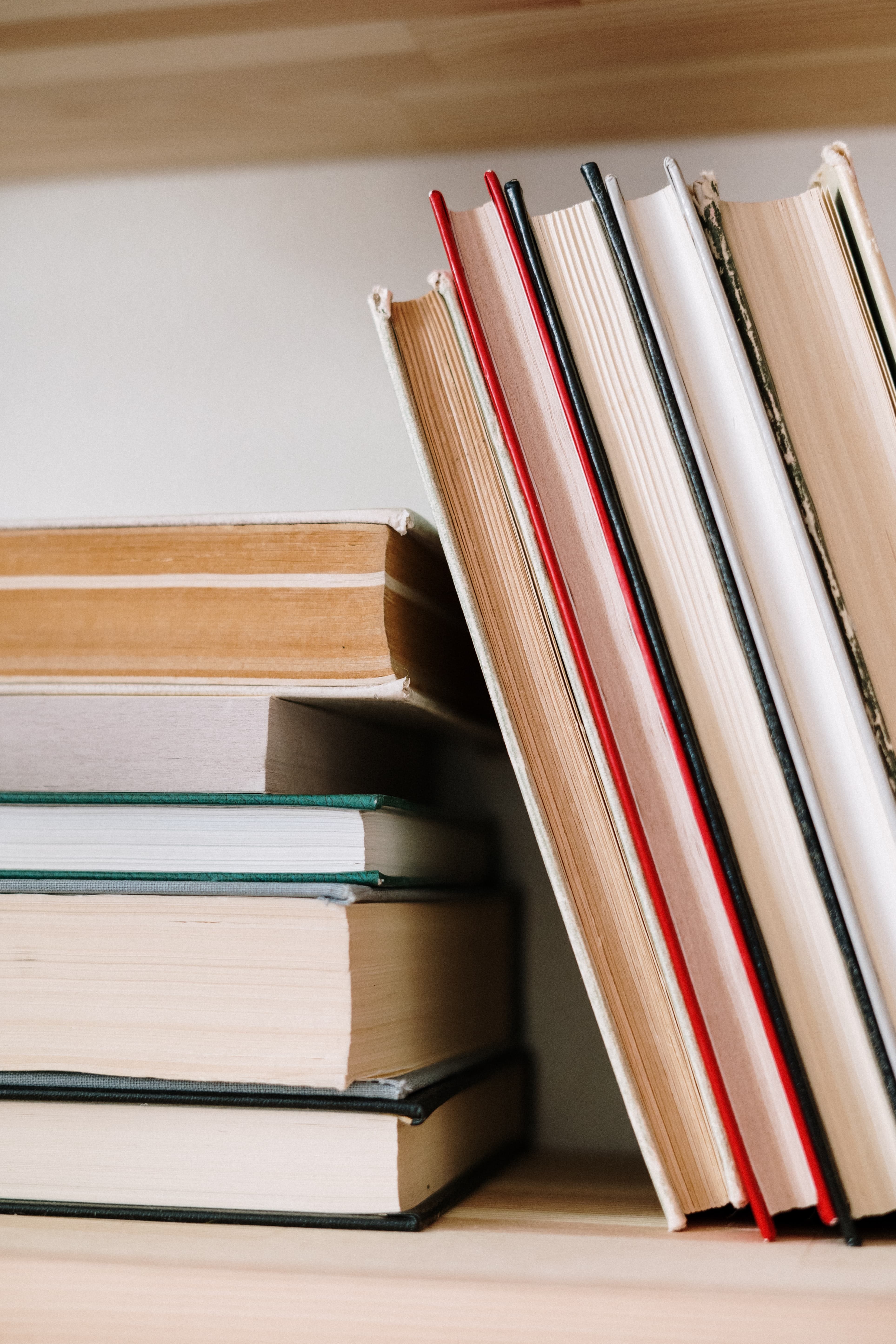 A close up photo showing several books stacked and leaning against each other, with their spines facing the wall. 