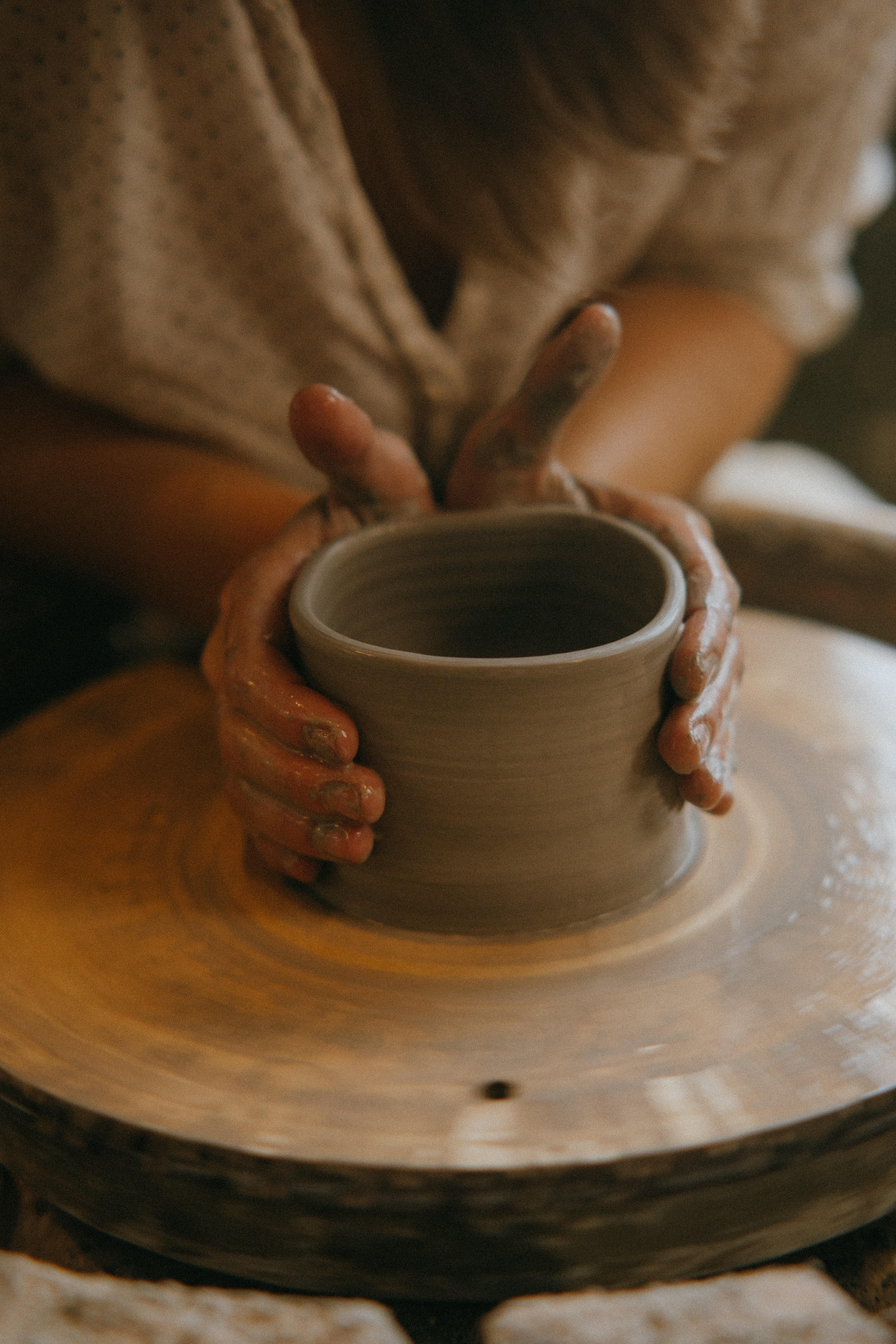 An image of someone using a pottery wheel to form a clay bowl. We can only see the person from the shoulders to their hands. 