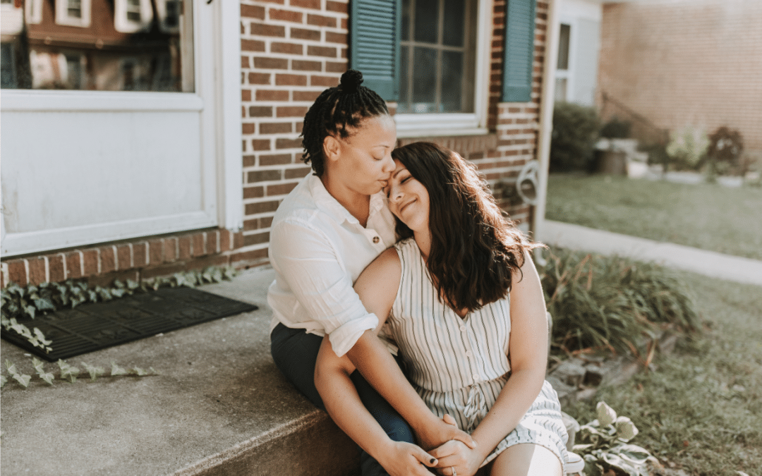 Two women cuddling together on a front stoop.