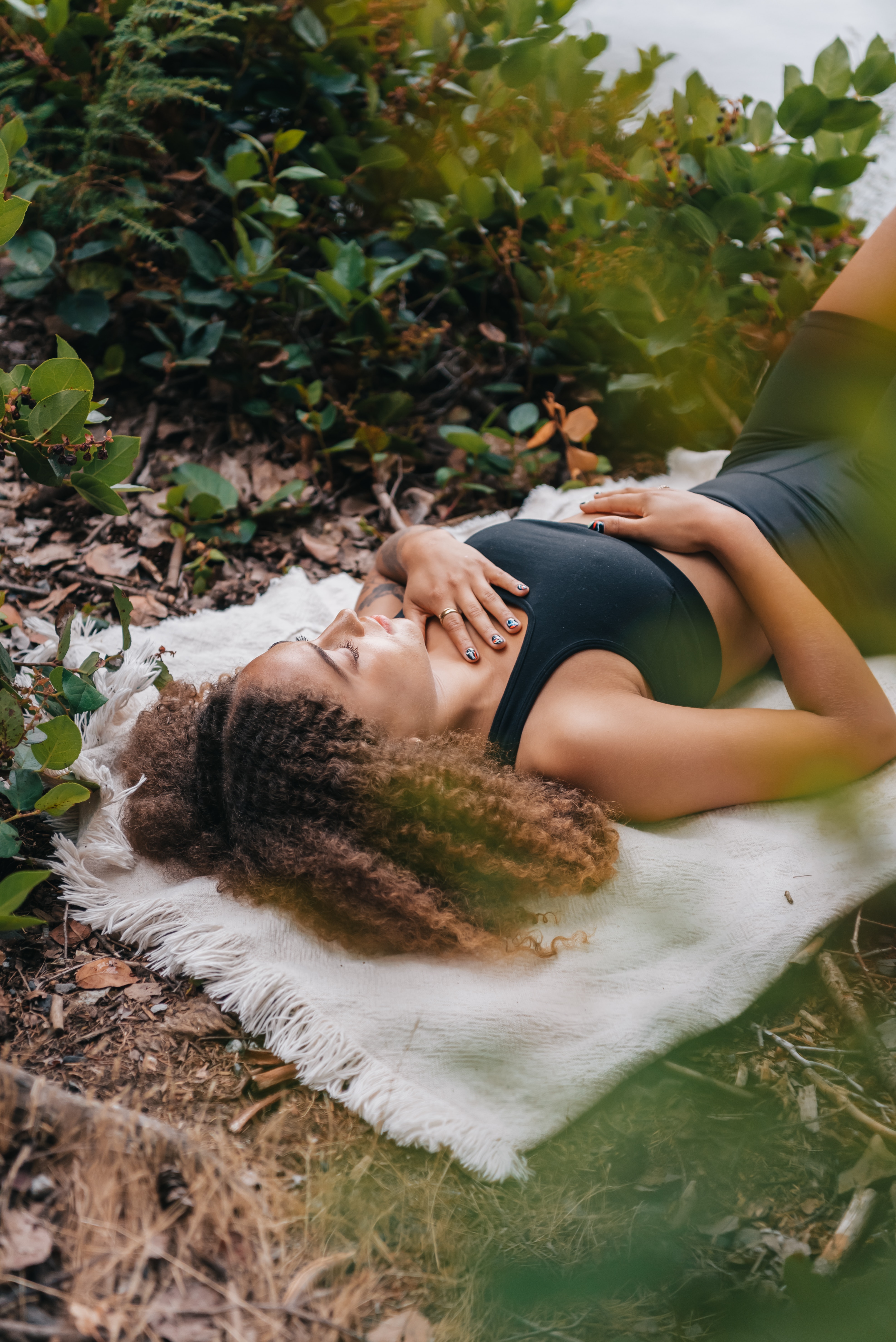 Stock image of woman relaxing in a park, lying down with one hand on belly and other on chest.