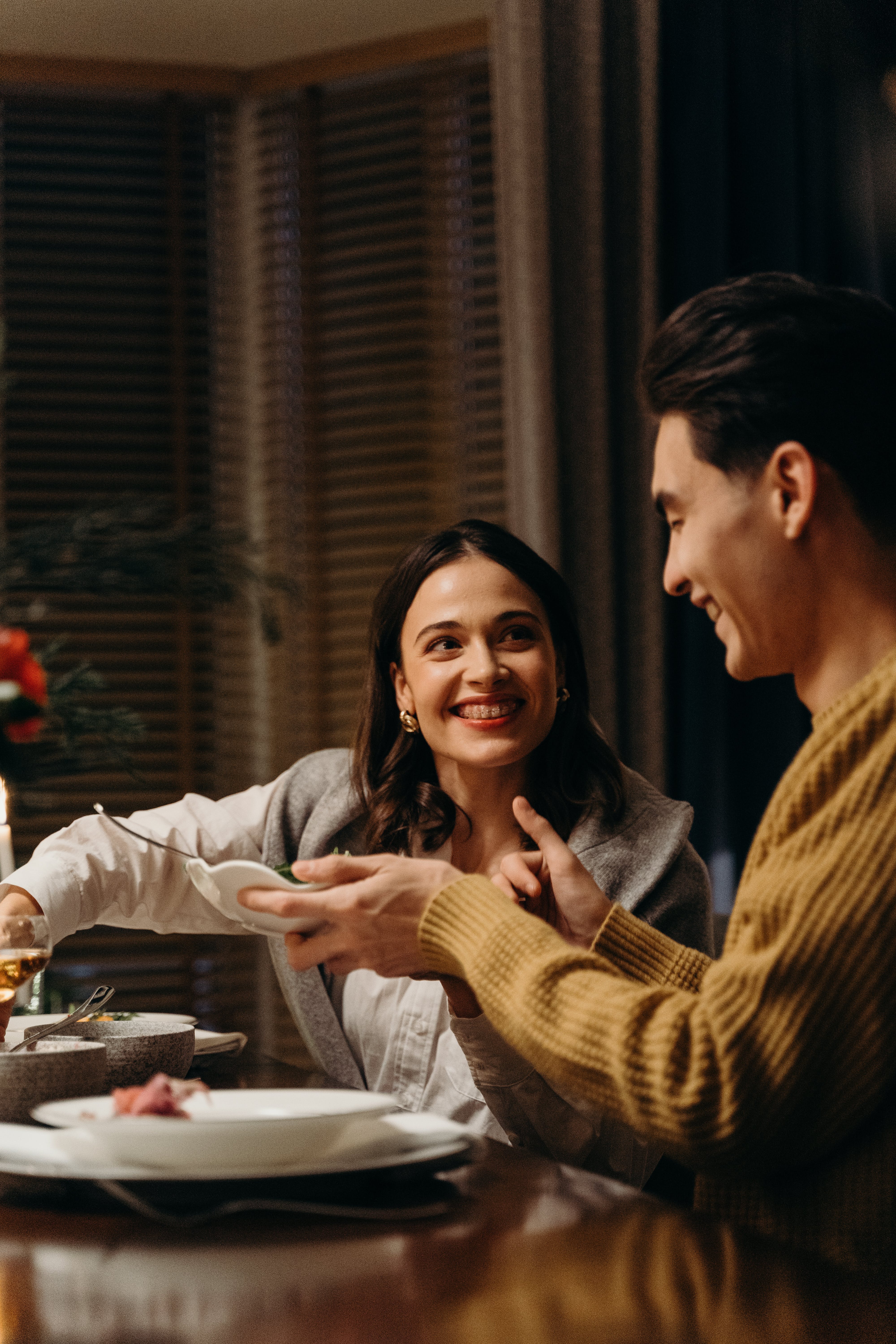 A woman serving herself from a large dish at the dinner table while smiling at the man next to her