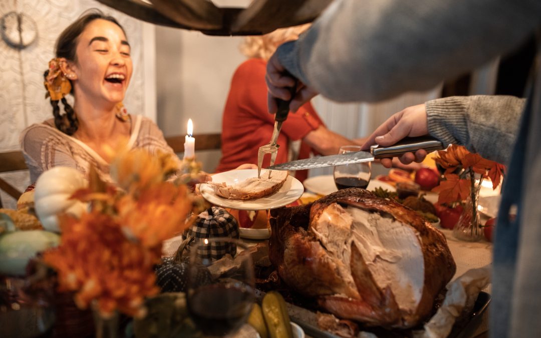 A young woman in braids laughing as someone cuts the turkey in front of her