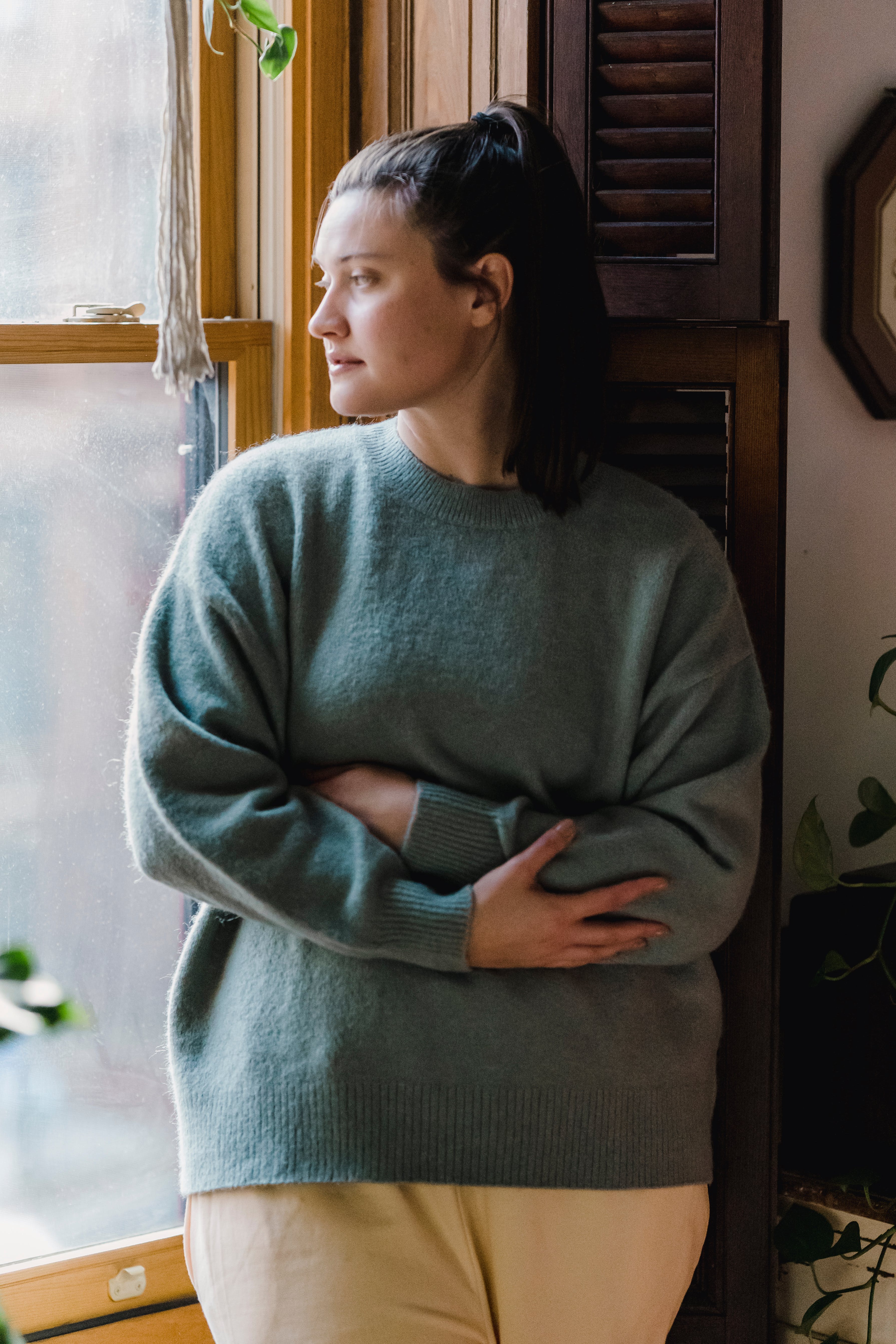 A woman holding herself and looking out of the window with a contented look on her face. 