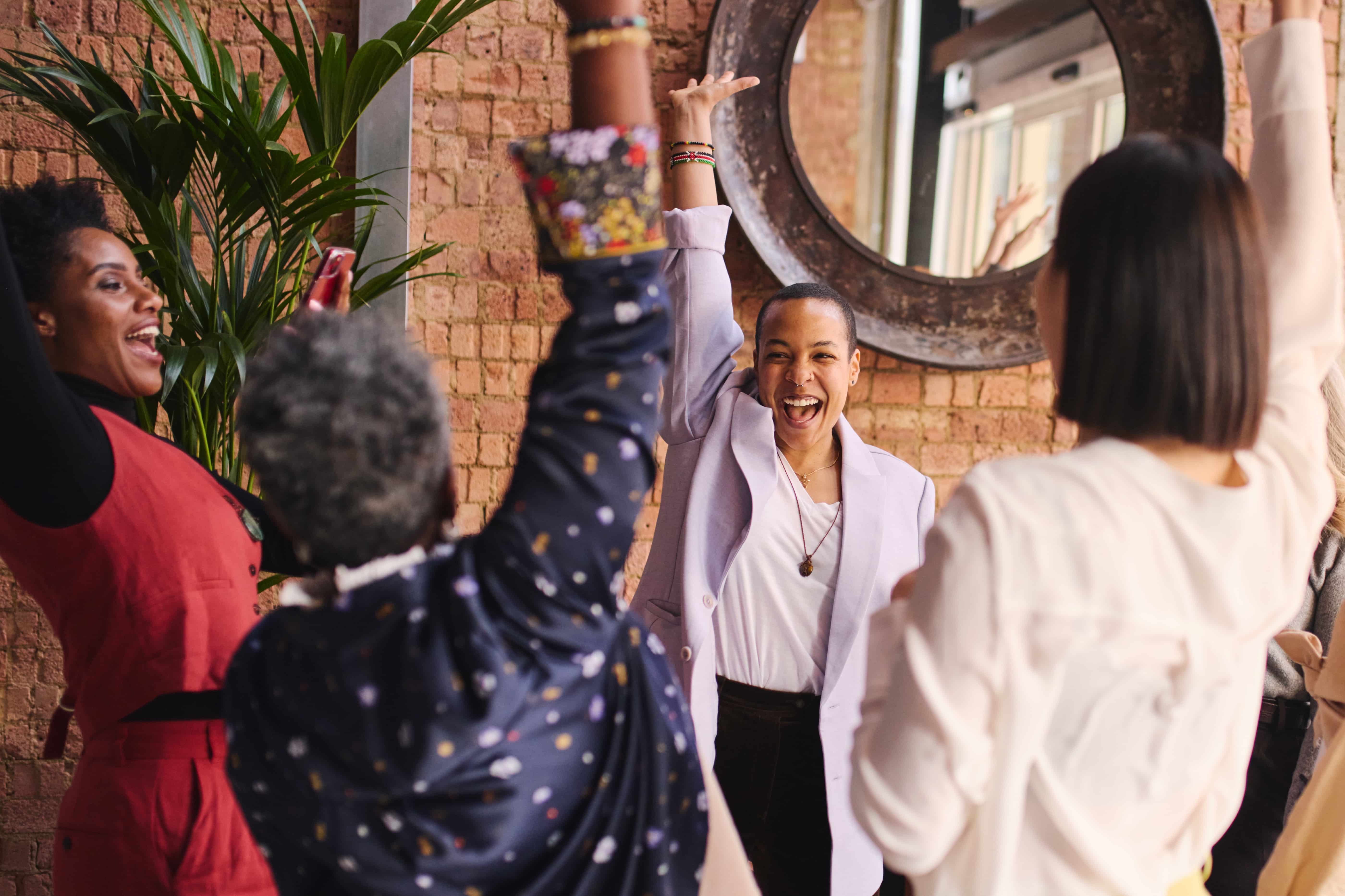 A group of young Black women raising their hands to high five/celebrate one another