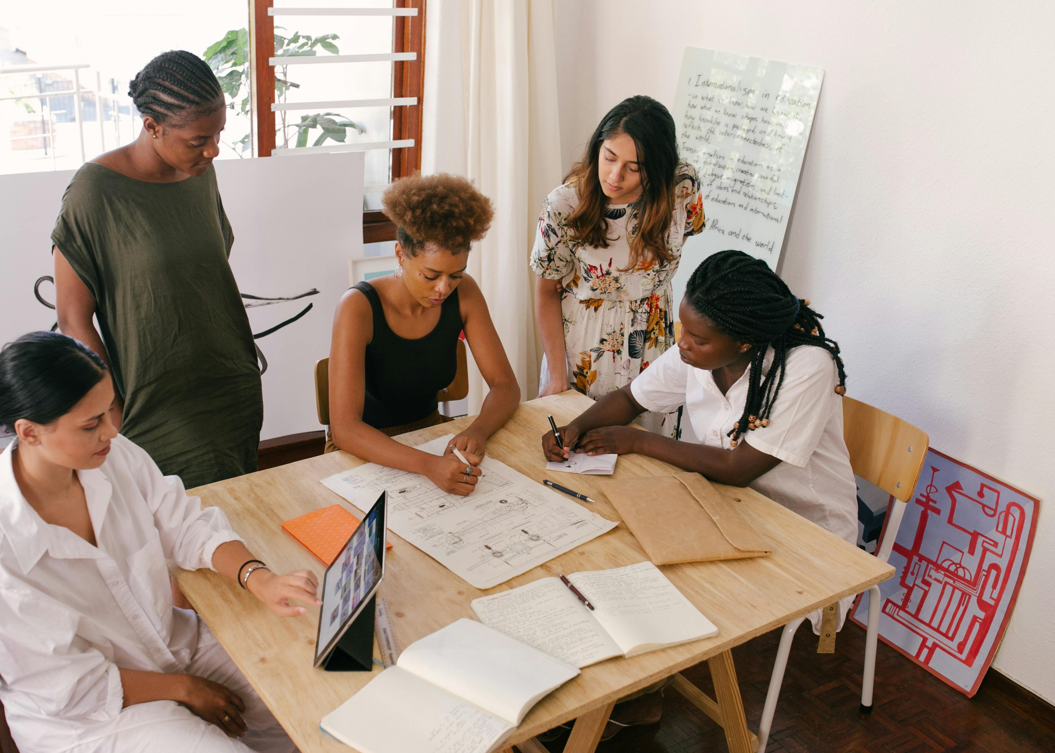 a group of women of color gathered around a conference table looking over their work