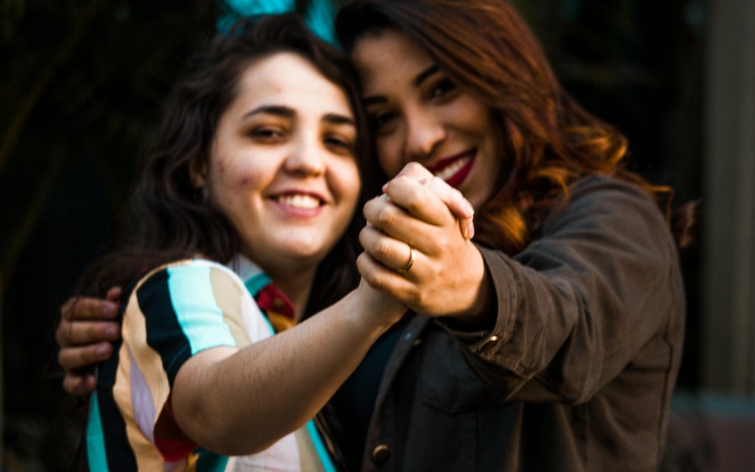 Two queer women of color smiling and dancing together