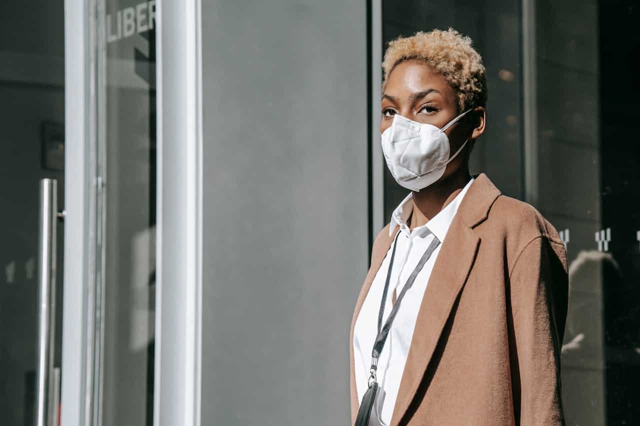 A Black woman in business casual attire wears a mask to protect herself from Covid.