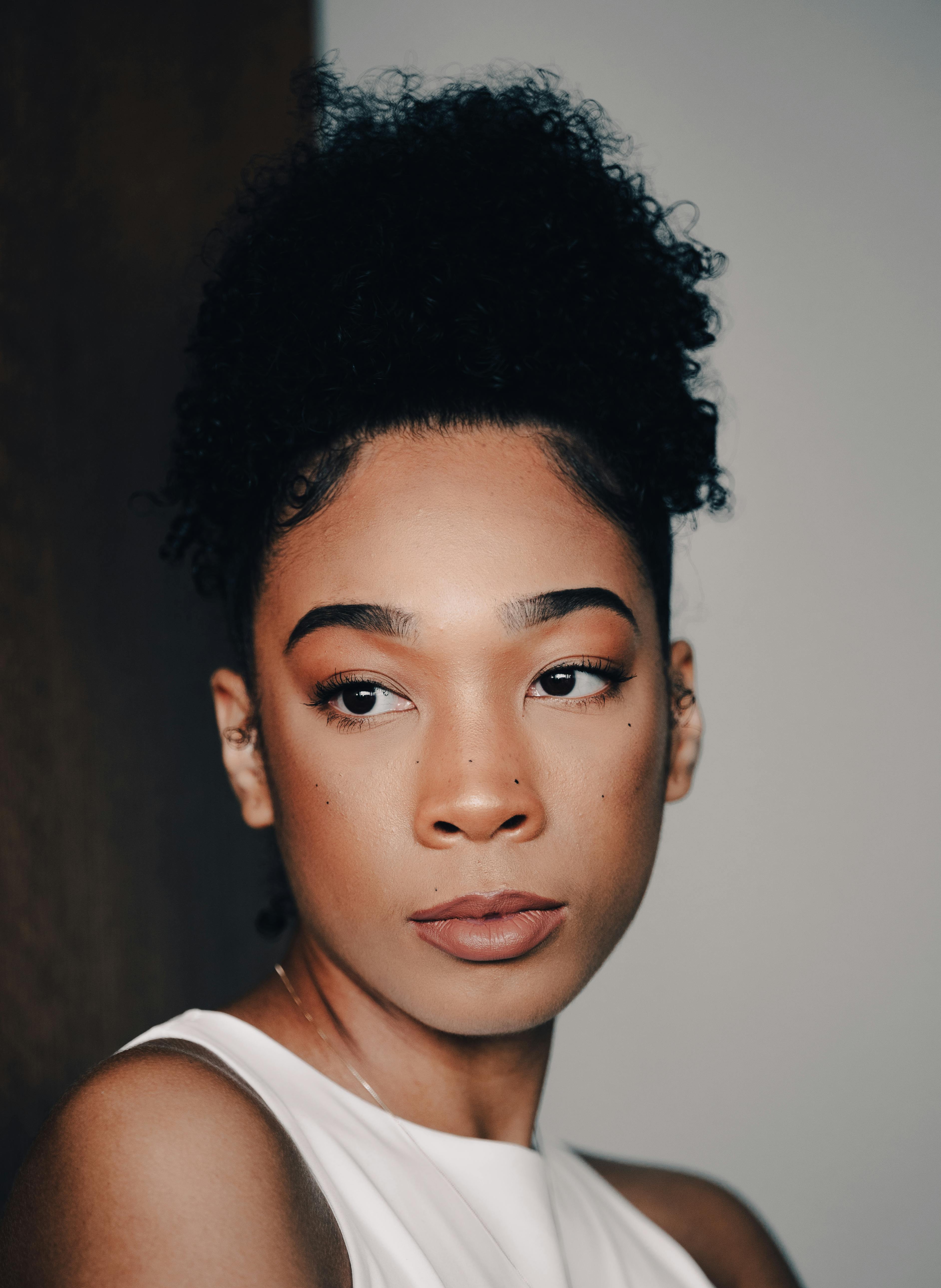 A portrait of a woman with medium complexion and dark natural curly hair tied up, looking off center. 