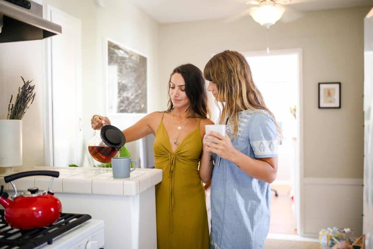 A bisexual couple, two women, making coffee together in a light and airy looking kitchen.