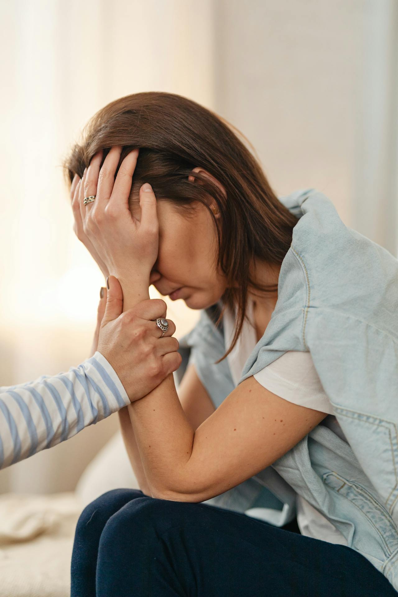 Woman with her head in her hands is comforted. 