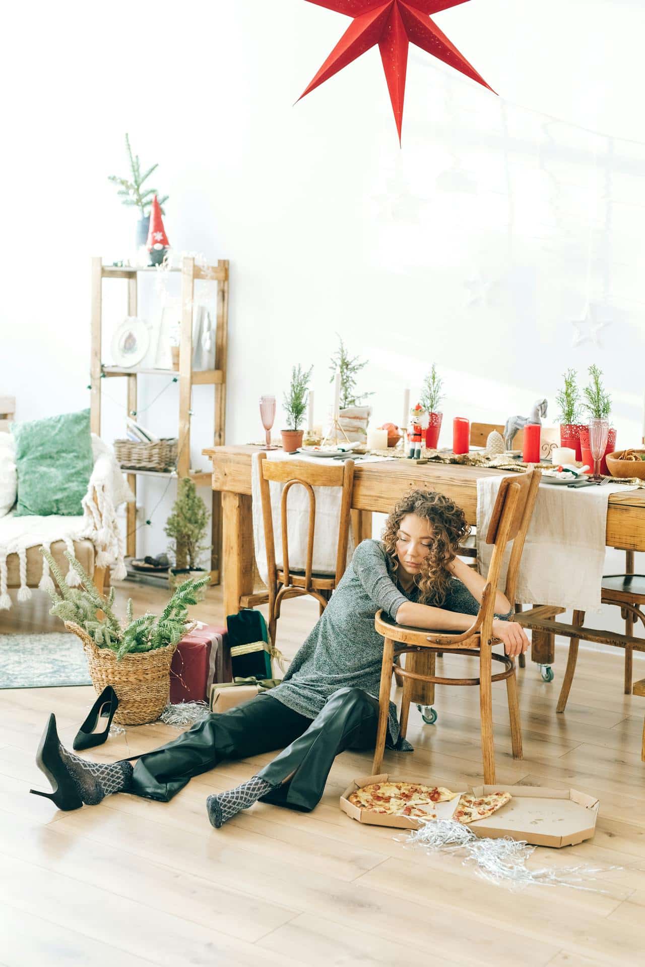 A tired-looking black woman with curly hair sits on the ground with holiday decor around her. 