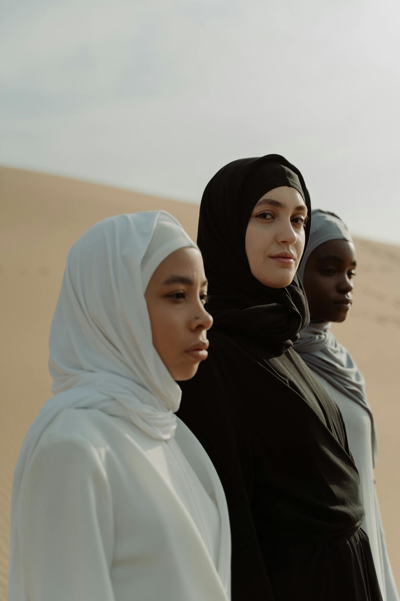 Three diverse women wearing hijabs standing in a desert, looking confidently toward the horizon