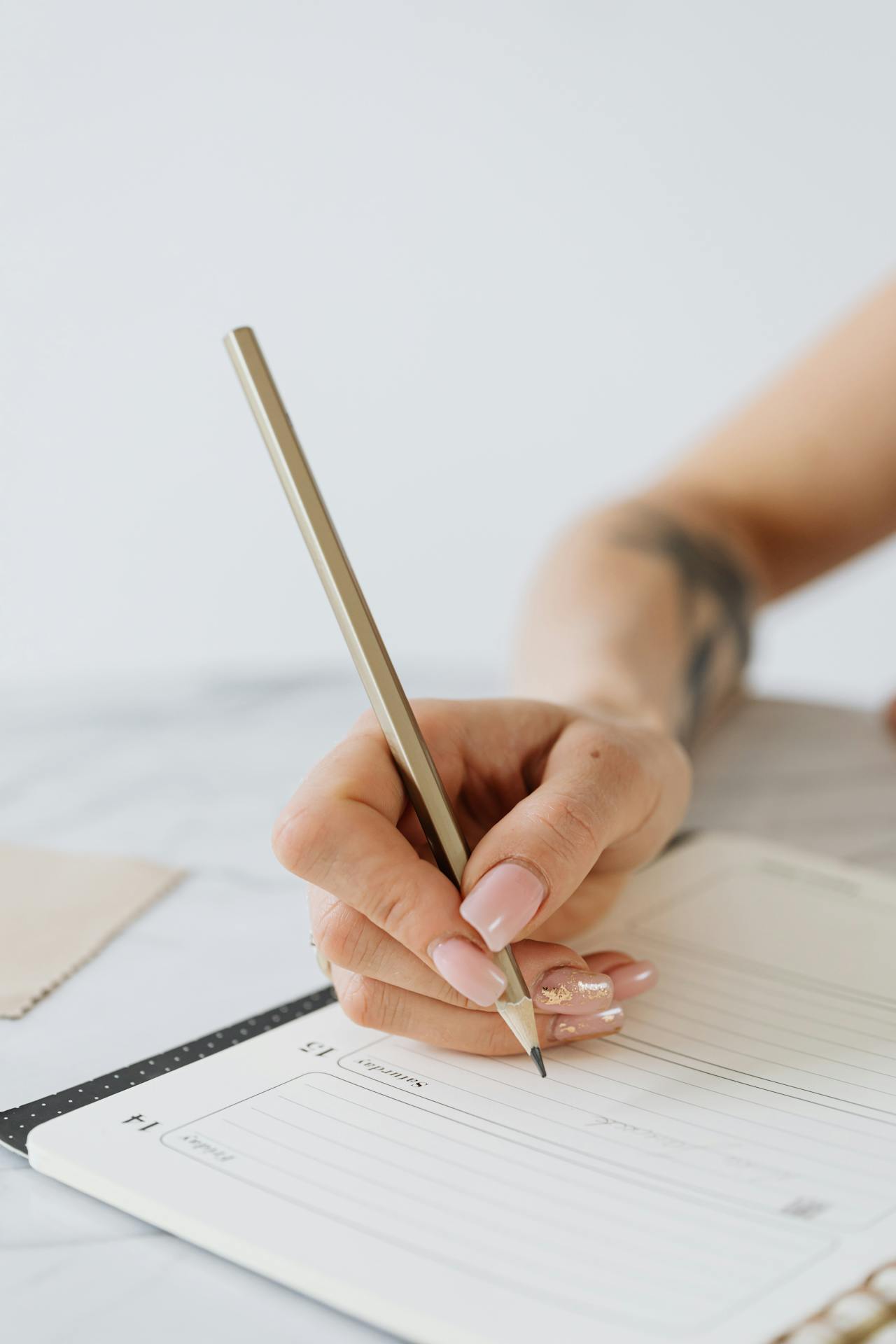 A hand with manicured cream-colored nails and holding a pencil writes on calendar.