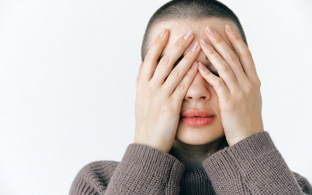 A woman with a shaved hairstyle holds her hands over hair face.