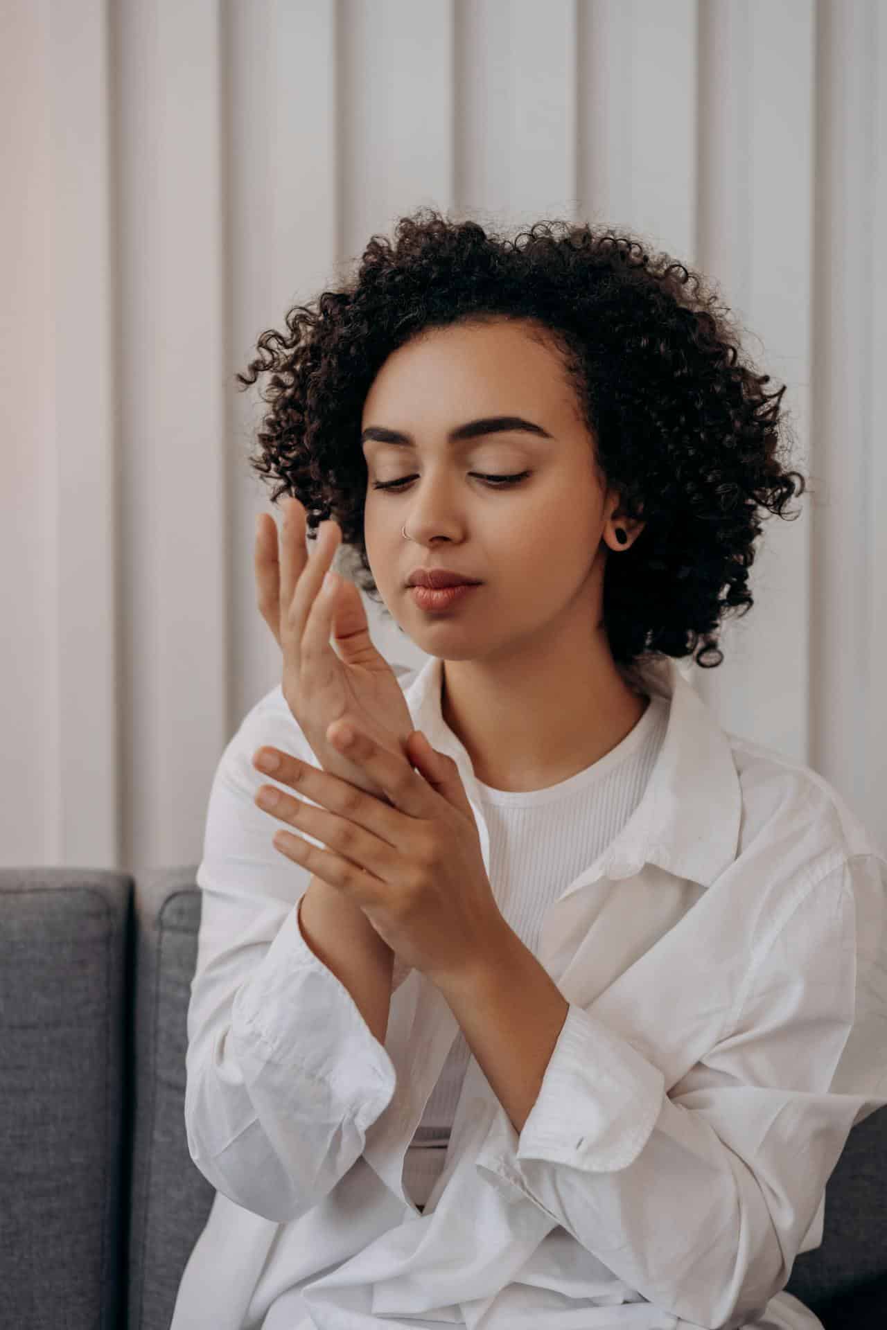 A black woman with curly hair and wearing a white blouse closes her as she puts her hands together.