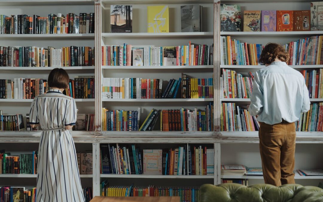 A man and a woman stand with their backs turned in front of a bookshelf.